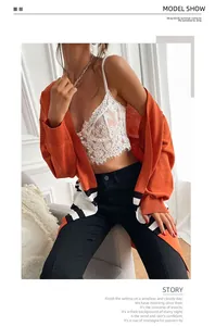 Detail of white floral lace bralette with eyelash trim under an orange knit cardigan