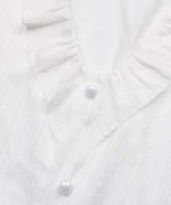 Détail macro du t-shirt blanc texturé avec col à volants et boutons nacrés