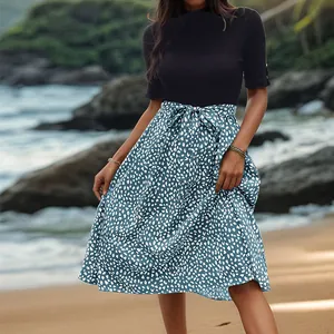 Tenue d'été femme avec haut en maille noir et jupe midi fleurie bleue sur la plage