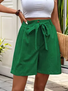 Detail of high-waist green shorts with textured fabric, wood button, and tied waist belt