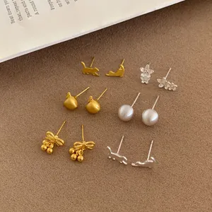 Set of six gold and silver flower and cat stud earrings on a textured fabric backdrop