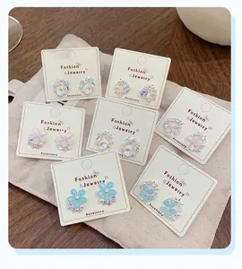 Dettaglio di sette orecchini a fiori con petali pastello e perle su cartoncino
