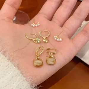 Three-piece gold earring set featuring pearls, hearts, and cat charms held in hand