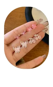 Detailaufnahme des Ohrring-Sets mit rosa Kirschblüten und Schmetterlingen auf der Hand