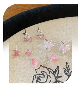 Detail von Kirsch-, Schmetterlings- und Blumen-Ohrringen in Rosa auf beigem Stoff
