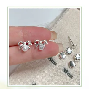 Detail of silver bow earrings with faux pearl and twin heart pendant jewelry close-up