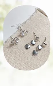 Detailed shot of silver bow pearl earrings and triple heart drop earrings on linen cloth
