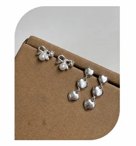 Detail showing bowknot pearl earrings and triple heart drop earrings on a paper box