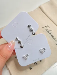 Detailed shot of silver heart drop earrings and bow stud with pearl on display card