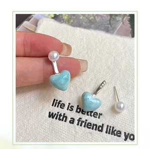Detail of light blue heart earrings with marble texture, white pearl and silver needle