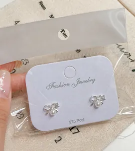 Detail of silver bow pearl earrings on a display card with jewelry care icons