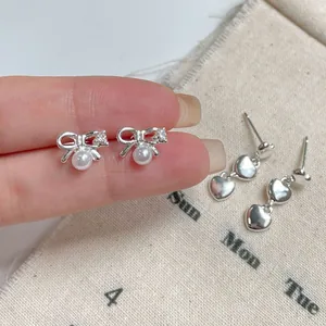 Minimalist silver bow pearl studs and triple heart drop earrings on linen background