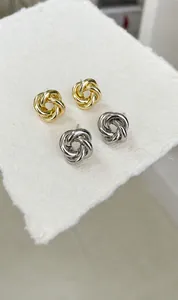 Détail de boucles d'oreilles nœuds métalliques argentées et dorées sur papier texturé