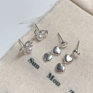 Bow pearl stud earrings and triple heart drop earrings on a linen background texture