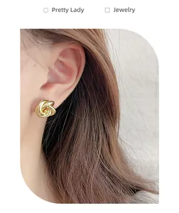 Gros plan de boucles d'oreilles nœud doré portées, montrant la texture et le design torsadé