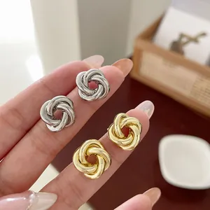 Boucles d'oreilles nœuds entrelacés polis en fini or et argent portées à la main