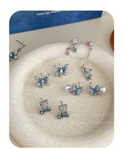 Detailed view of silver bear and butterfly stud earrings with sparkling blue rhinestones