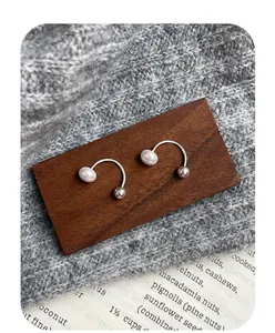 Detailed view of U-shaped ear cuff with white pearl and silver bead on wooden surface