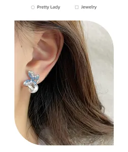 Detail of butterfly stud earring with blue rhinestones and dangling pearl on ear