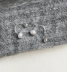 Detail of silver screw-back pearl earrings on a grey knit sweater background