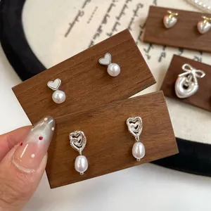 Eleganti orecchini a cuore in argento con perle bianche su un supporto di legno