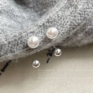Minimalist U-shaped pearl ear clips with silver metal beads on a grey knit background