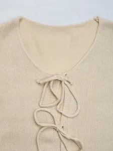 Detail of a beige knit cardigan featuring a round neckline and delicate tie-up bow closure