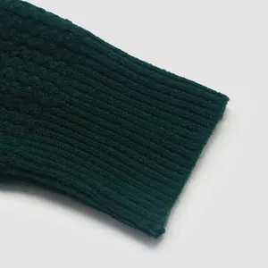 Close-up of dark green knitted sweater showing textured honeycomb and ribbed cuff detail