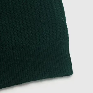 Macro detail of dark green honeycomb knit texture and ribbed hem on a cozy sweater
