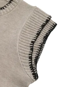 Dettaglio del gilet in maglia beige con cuciture nere a contrasto e scollo a costine