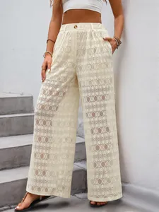 Détail du pantalon large en dentelle à taille haute avec motifs géométriques et bouton décoratif