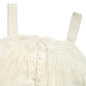 Detail of ivory textured cotton gauze romper featuring wide straps and button closure