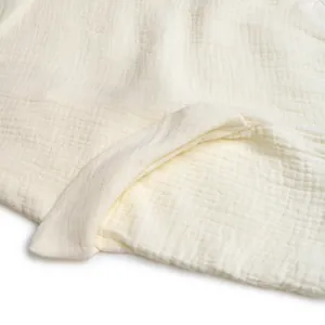 Close-up of cream textured muslin fabric showing soft double-layer gauze and stitched edge
