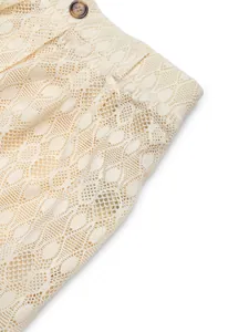 Gros plan du pantalon en dentelle beige avec texture ajourée et détail du bouton marbré