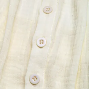 Close-up of textured cotton crepe fabric and white resin buttons on beige jumpsuit