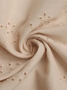 Gros plan du tissu du gilet beige avec broderie florale ajourée délicate et texture