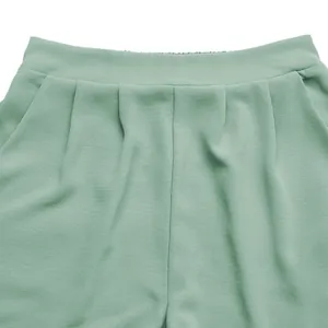 Detail of sage green elastic waist shorts featuring vertical pleats and side pockets