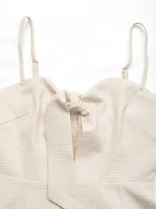 Detail of beige waffle textured playsuit featuring adjustable straps and front tie knot