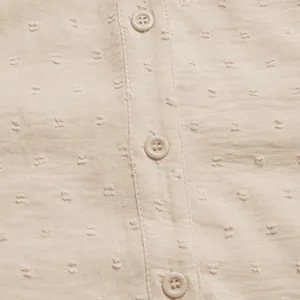 Macro detail of apricot swiss dot fabric and matching round buttons on the shirt placket