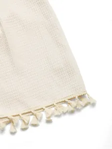 Detailed view of the ivory waffle weave fabric with woven fringe trim on the romper edge