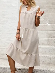 Dettaglio dello scollo a V con coulisse e nappe su un abito midi boho beige senza maniche