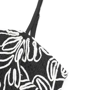 Detail of black textured fabric with white floral embroidery and adjustable thin strap