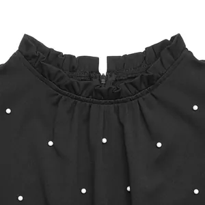 Dettaglio del collo alto a balze su tuta nera con eleganti decorazioni in perle bianche