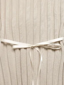 Détail de la maille côtelée beige avec un nœud en satin blanc lisse à la taille