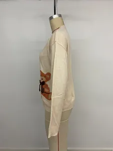 Détail du pull en maille montrant un jacquard d'ours et un nœud 3D rouge sur tissu beige