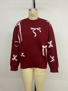 Detailed view of dark red knit sweater featuring white bow patterns and ribbed round neck