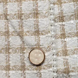 Macro-opname van tweed textuur met imitatieparels en een gouden metalen knoop op de jas
