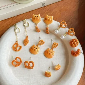 Set di orecchini a forma di croissant pretzel e gatto su un piatto bianco strutturato