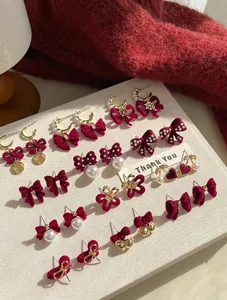 Detail of red velvet bow earrings with gold accents and pearls on a white display