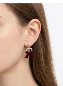 Close-up of model wearing velvet bow heart earrings with burgundy flocking and pearls